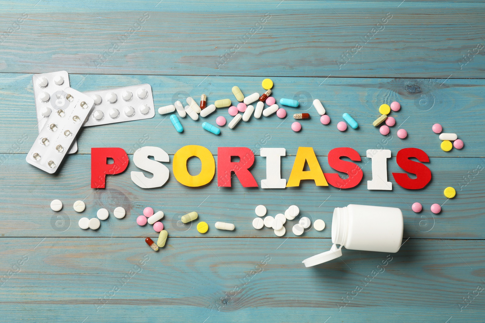 Photo of Word Psoriasis made of paper letters and pills on light blue wooden table, flat lay