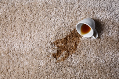 Overturned cup and spilled tea on beige carpet, top view. Space for text