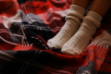 Woman in knitted socks on warm plaid, closeup. Space for text