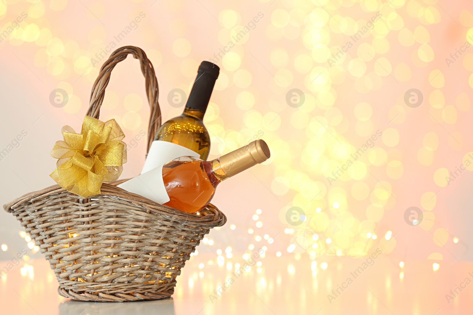 Photo of Wicker basket with bottles of wine against blurred lights. Space for text