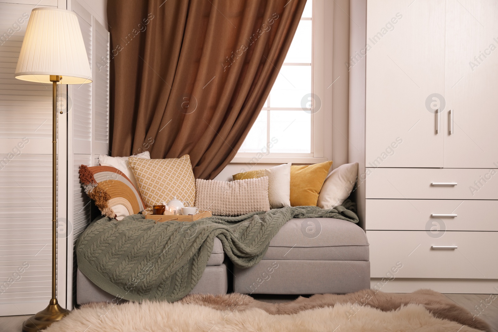 Photo of Comfortable lounge area with knitted blanket and soft pillows near window in room