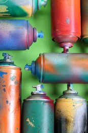 Many spray paint cans on green background, flat lay
