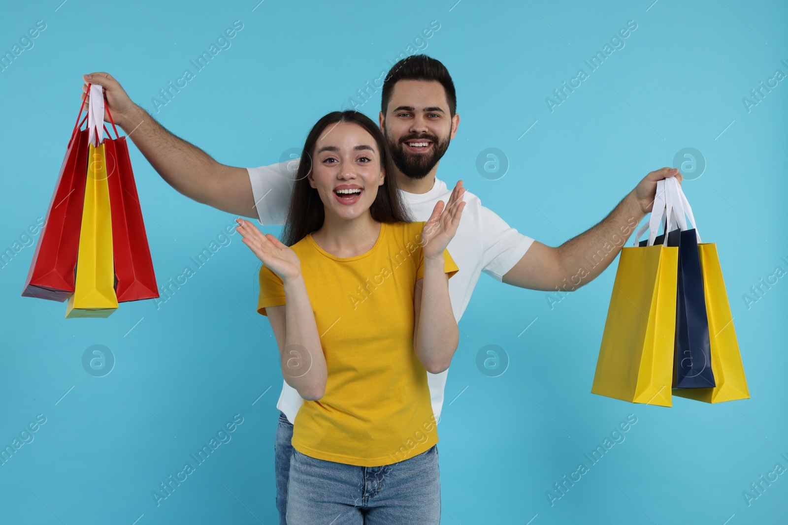 Photo of Excited couple with shopping bags on light blue background