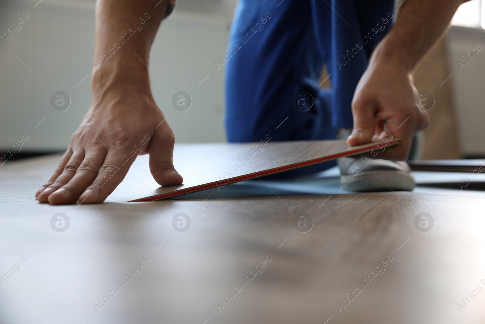 Photo of Worker installing laminated wooden floor indoors, closeup