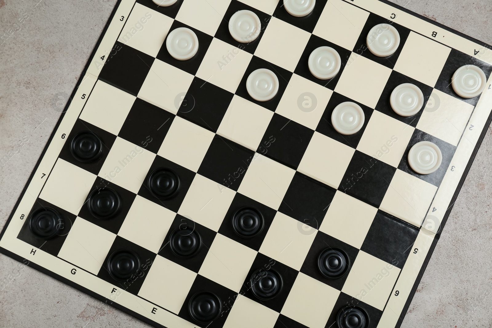 Photo of Checkerboard with game pieces on light grey table, top view