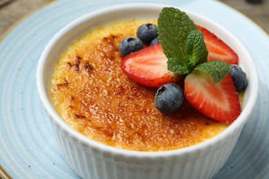 Delicious creme brulee with berries and mint in bowl on plate, closeup