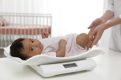 Doctor weighting African-American baby on scales in light room