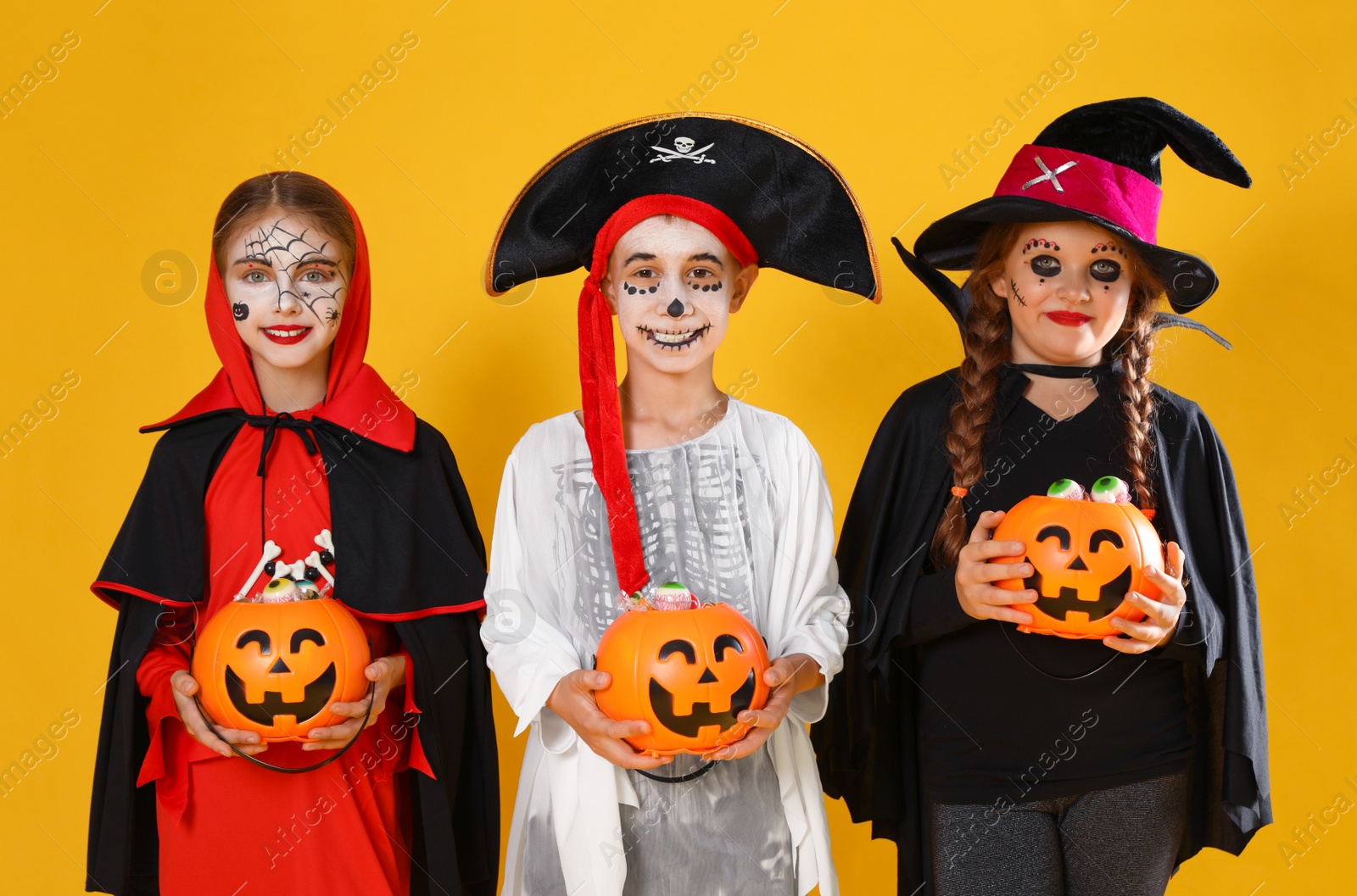 Photo of Cute little kids with pumpkin candy buckets wearing Halloween costumes on yellow background