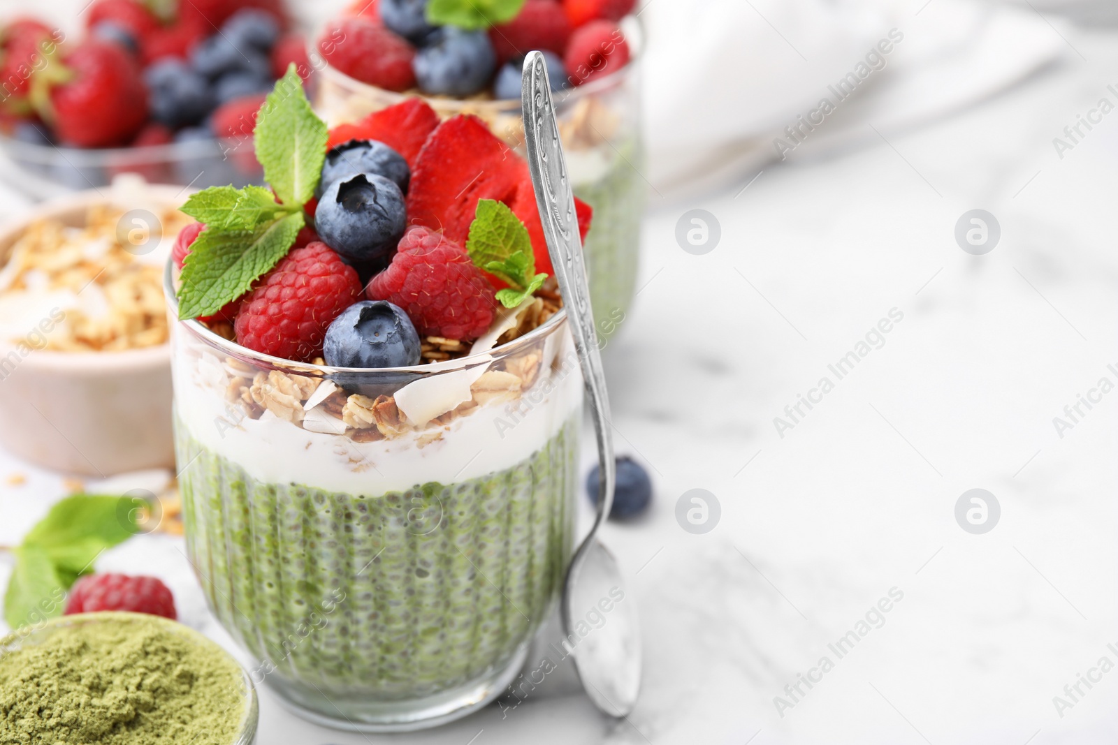 Photo of Tasty matcha chia pudding with oatmeal and berries on white marble table, closeup. Space for text. Healthy breakfast