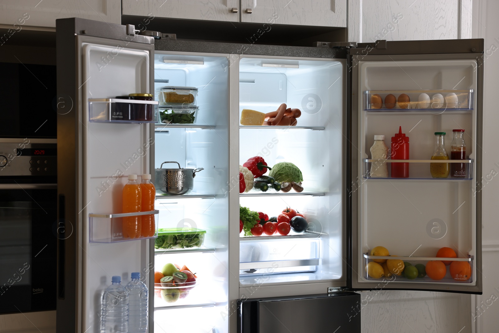 Photo of Open refrigerator full of different products in kitchen