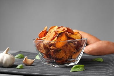 Photo of Bowl of sweet potato chips and garlic on table against grey background