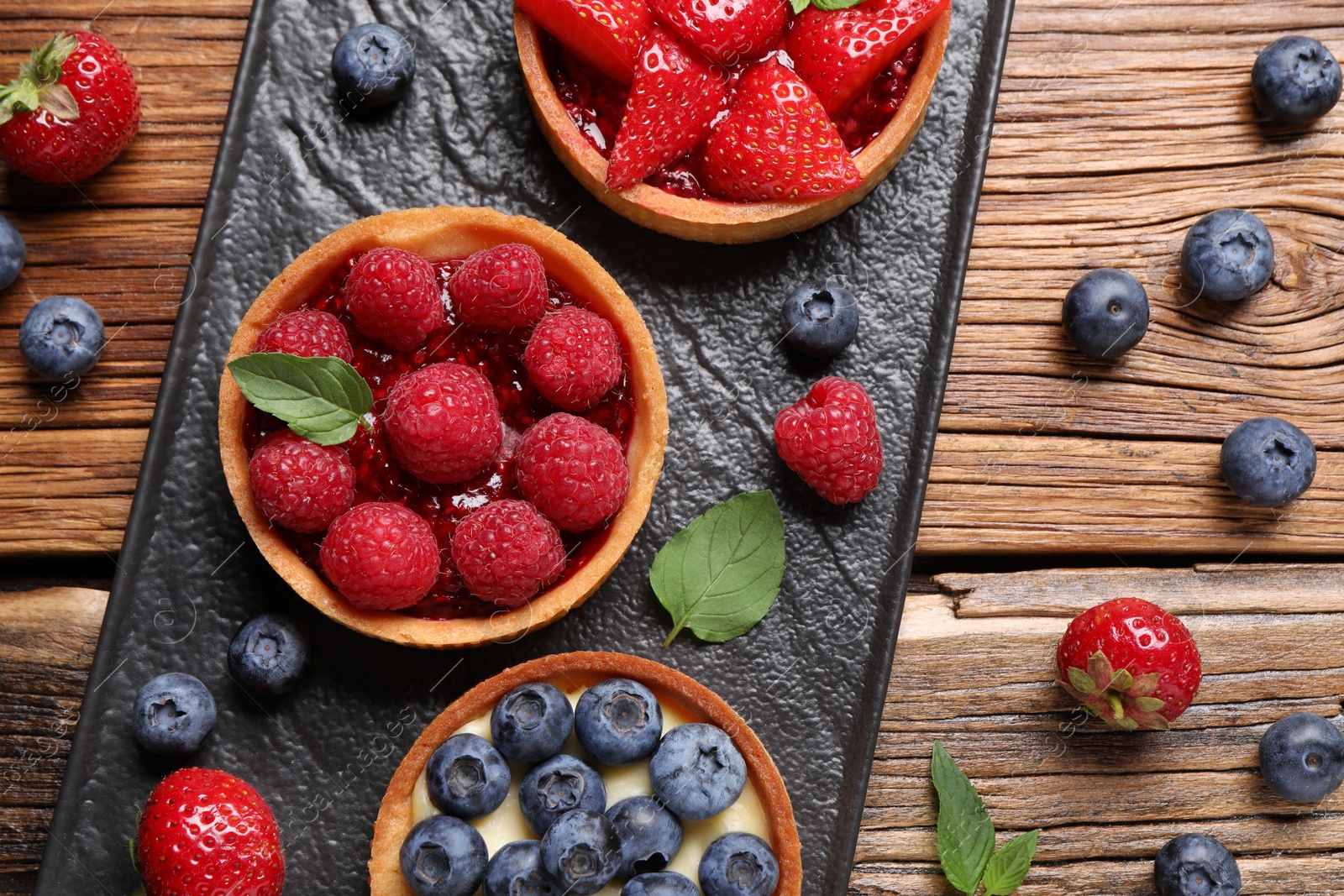 Photo of Tartlets with different fresh berries on wooden table, flat lay. Delicious dessert