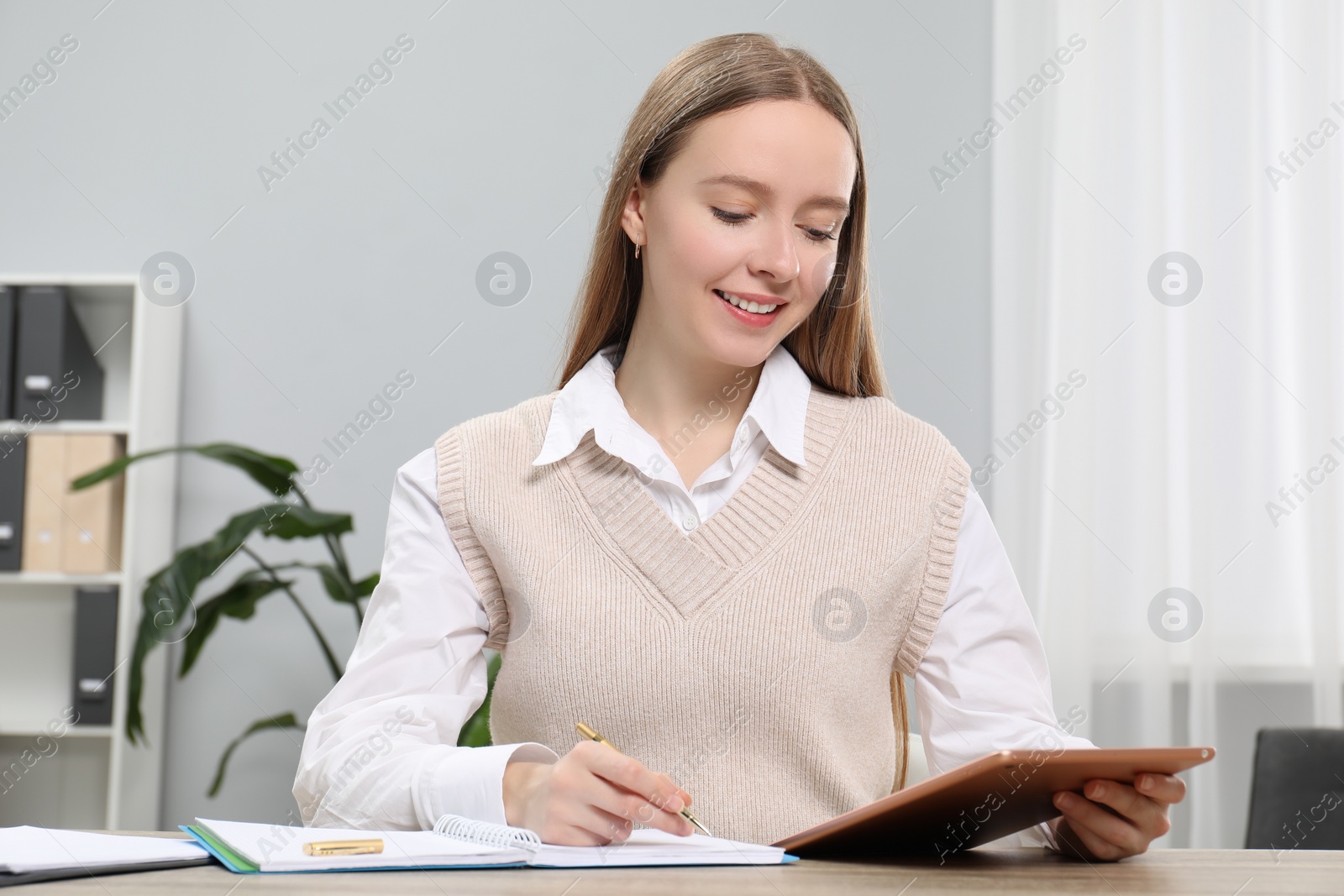 Photo of Woman taking notes while using tablet at table in office