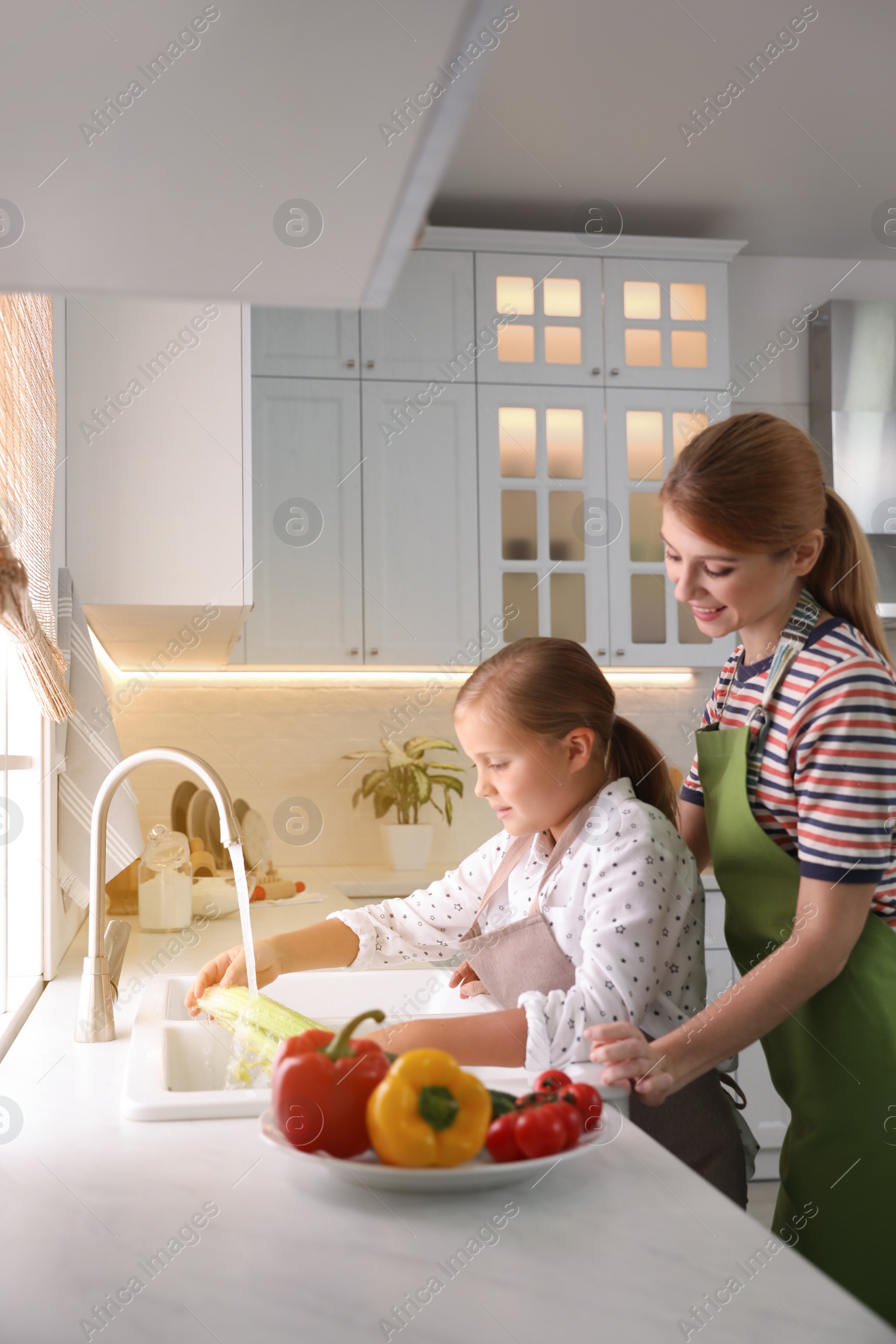 Photo of Mother and daughter washing vegetables in kitchen
