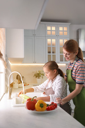Mother and daughter washing vegetables in kitchen