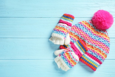 Warm knitted hat and mittens on blue wooden background, flat lay. Space for text