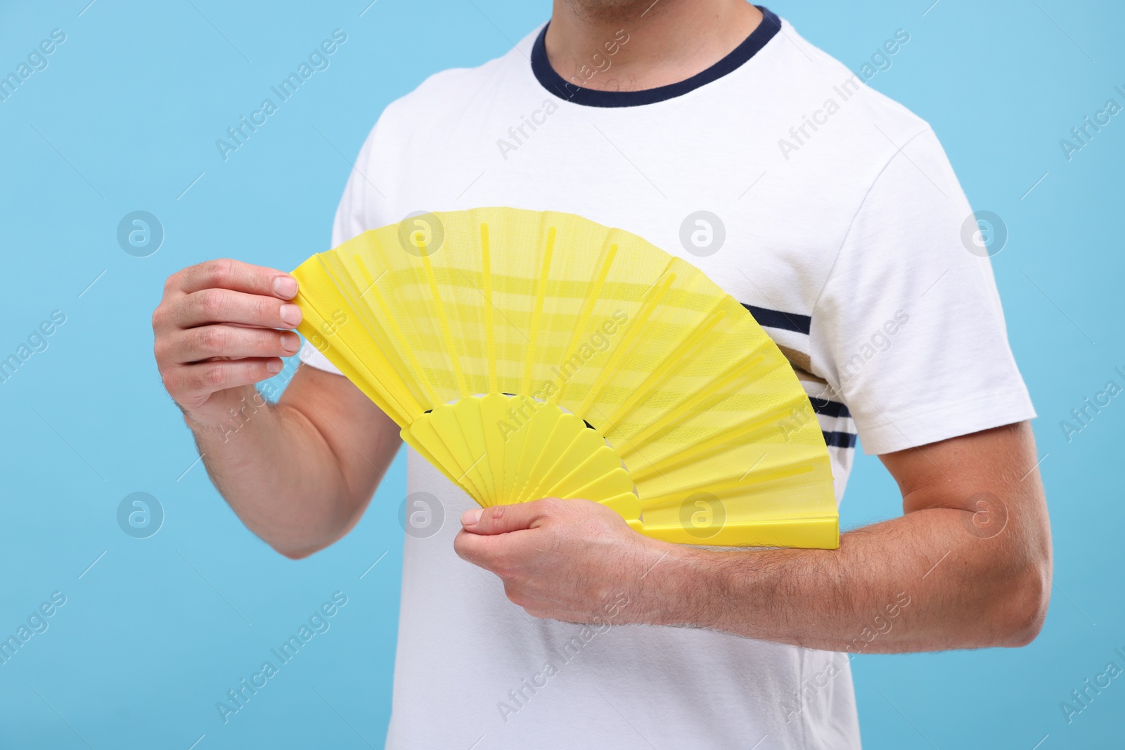 Photo of Man holding hand fan on light blue background, closeup