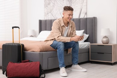 Photo of Smiling guest with smartphone on bed in stylish hotel room