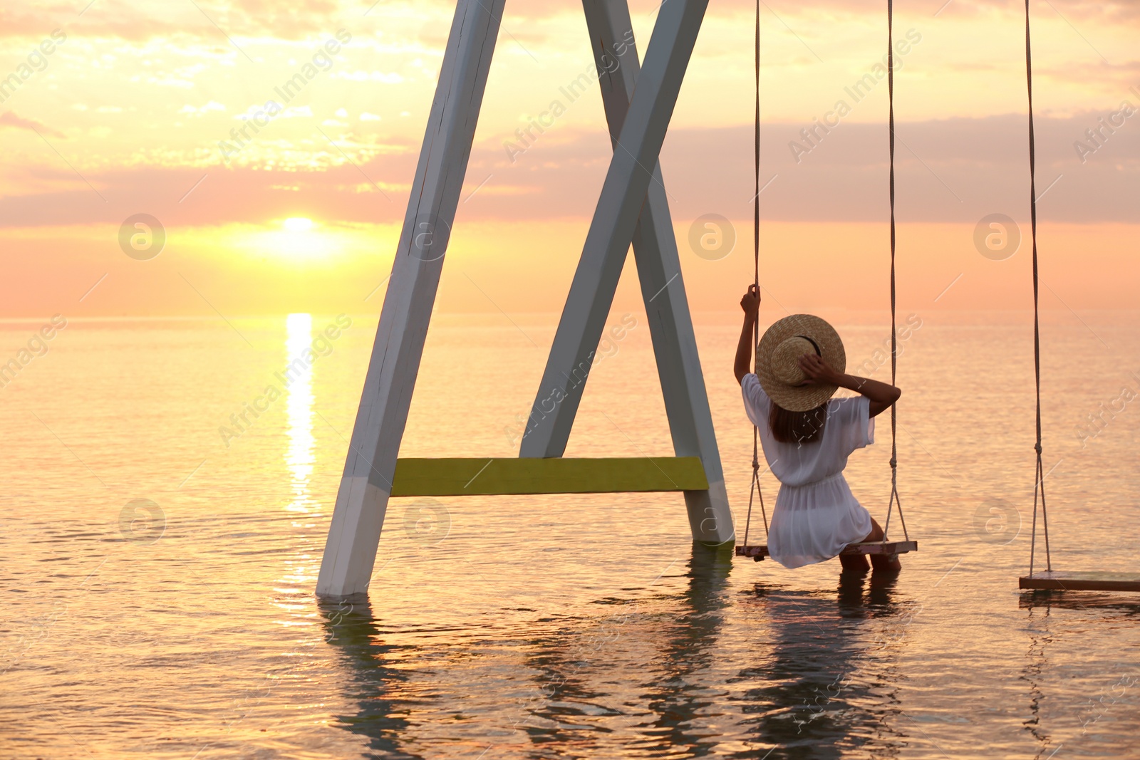 Photo of Young woman enjoying sunrise on swing over water