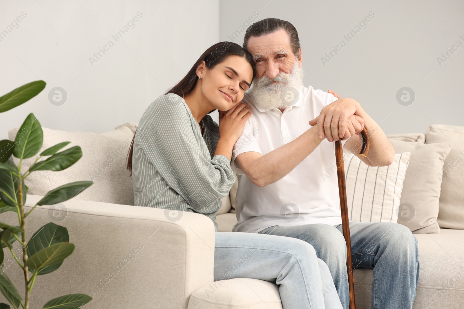 Photo of Senior man with walking cane and young woman on sofa indoors