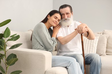 Photo of Senior man with walking cane and young woman on sofa indoors