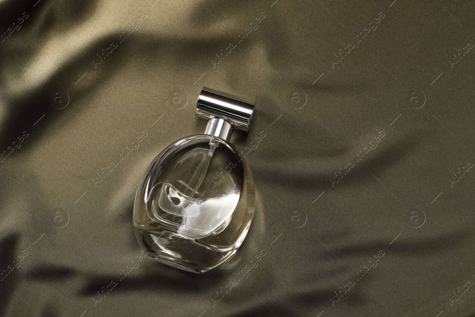 Photo of Luxury perfume in bottle on dark silk fabric, top view