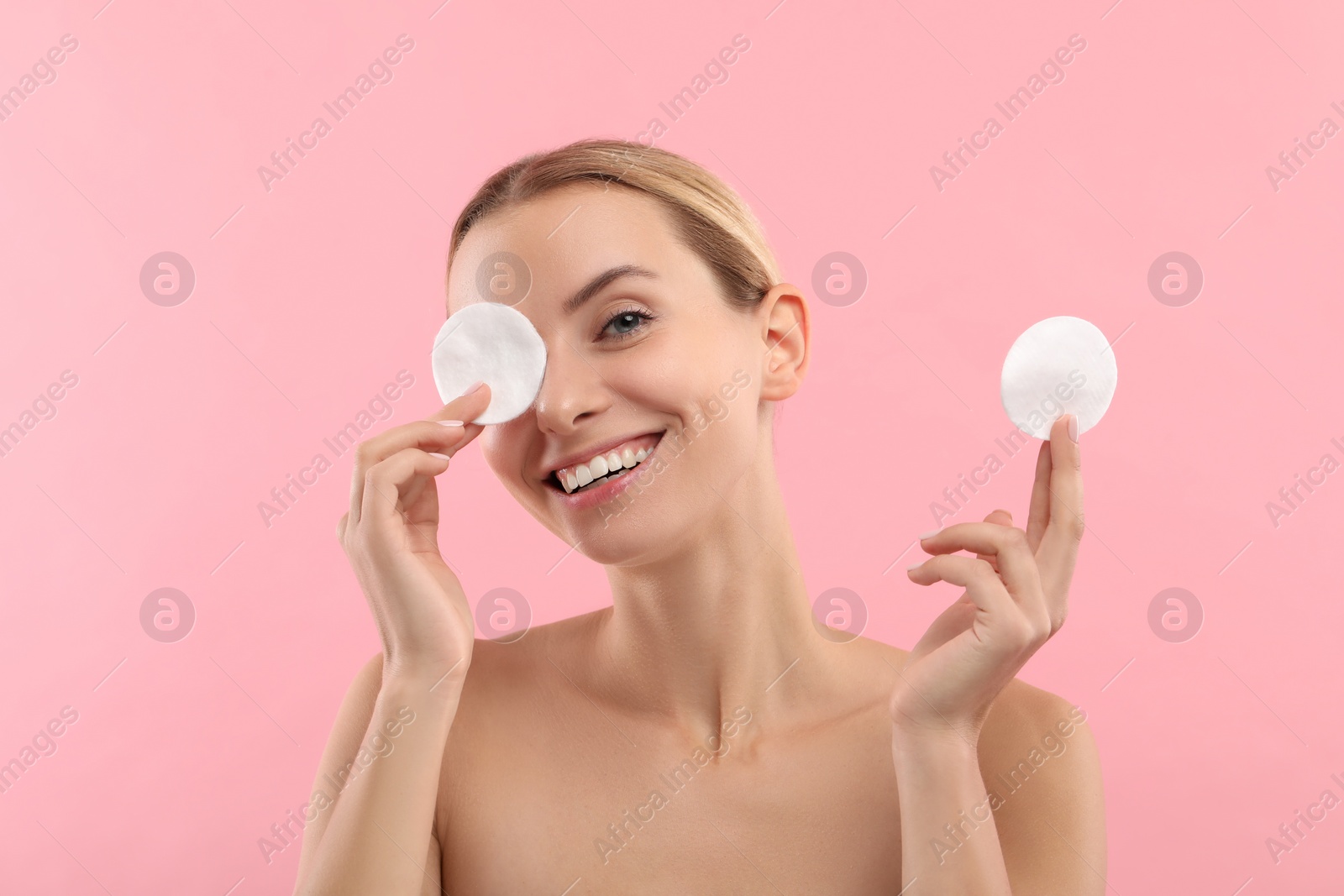 Photo of Smiling woman removing makeup with cotton pads on pink background