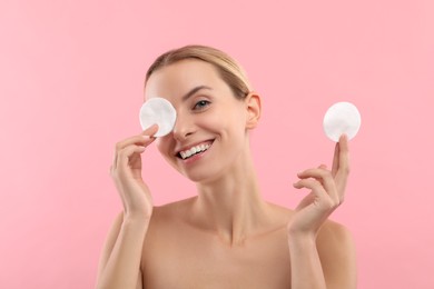 Smiling woman removing makeup with cotton pads on pink background