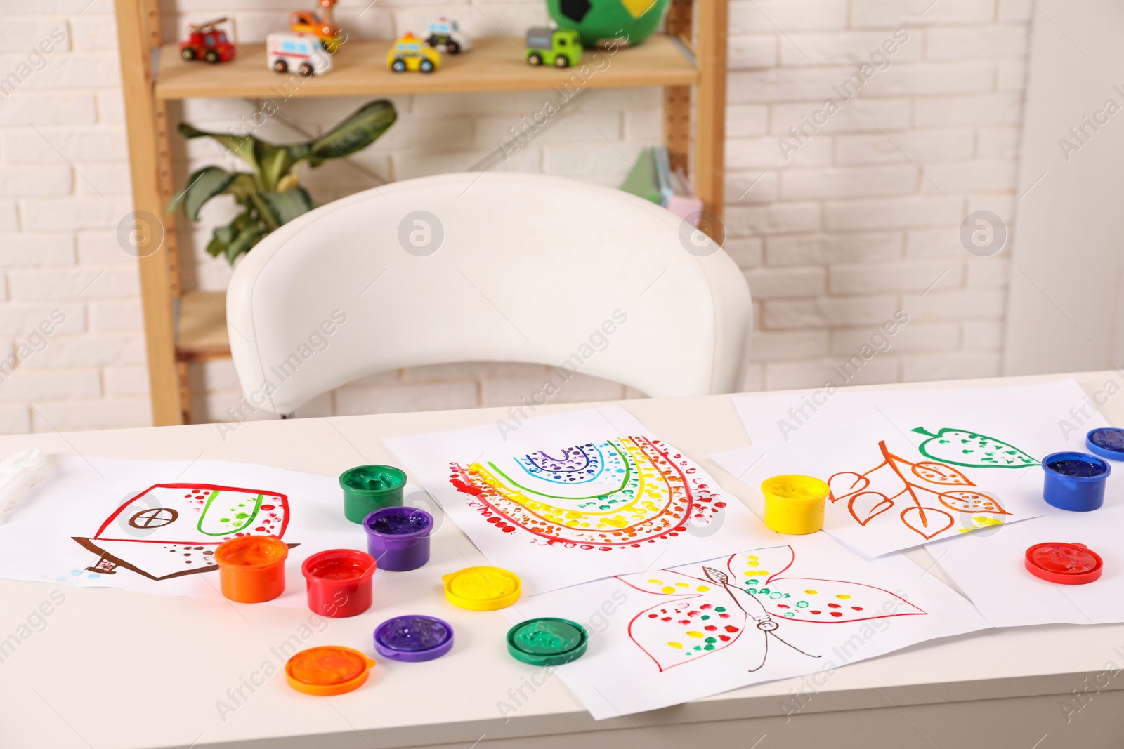 Photo of Cute children's drawings and set of paints on white table in room