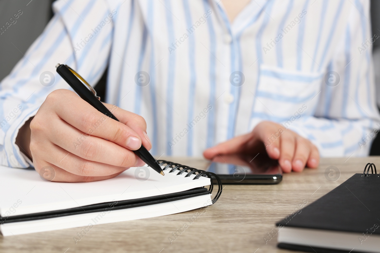 Photo of Woman writing in notebook at wooden table indoors, closeup