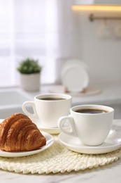 Photo of Breakfast served in kitchen. Cups of coffee and fresh croissant on white table