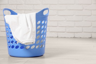 Photo of Laundry basket with clothes near white brick wall. Space for text