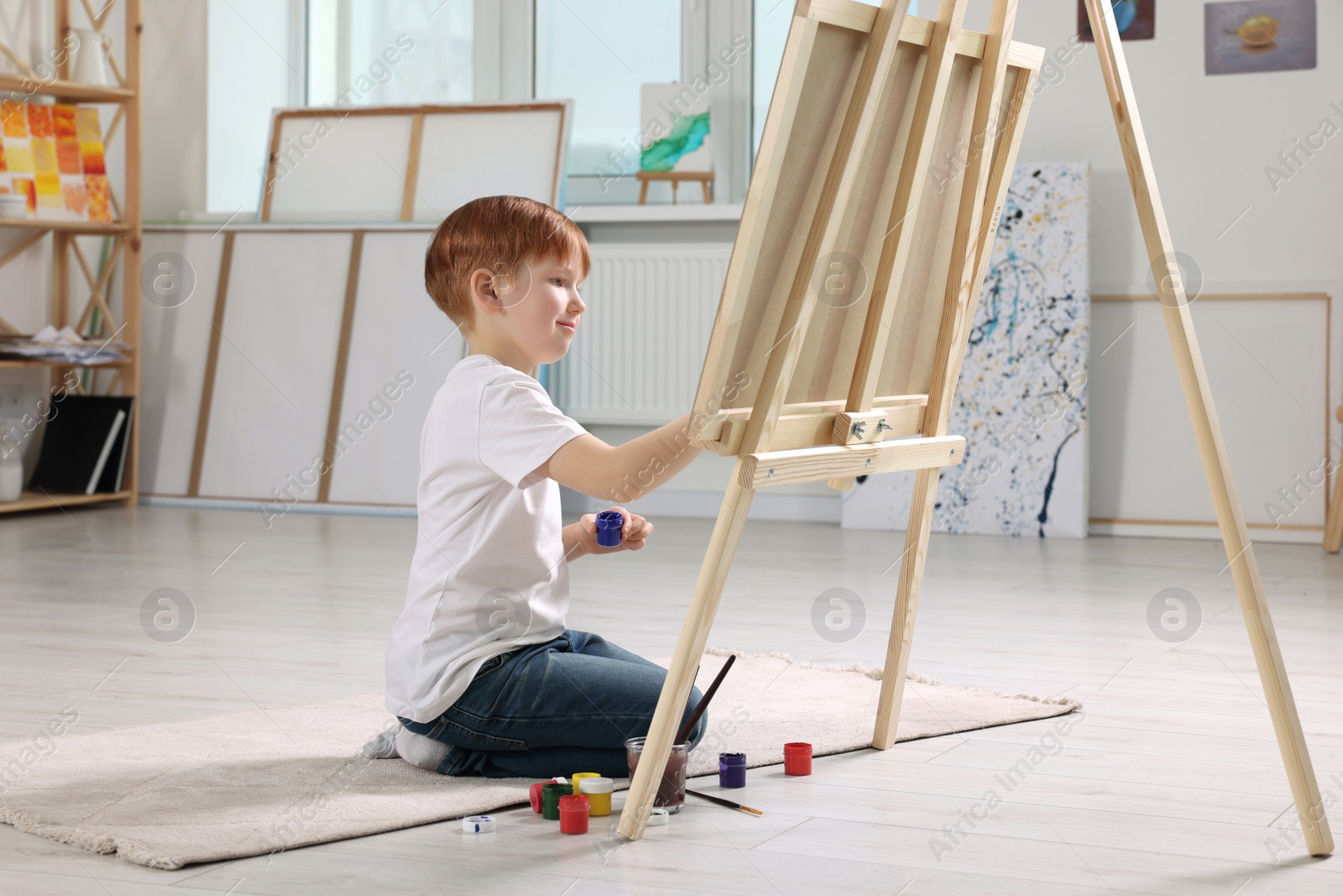 Photo of Little boy painting in studio. Using easel to hold canvas