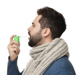 Young man with scarf using throat spray on white background