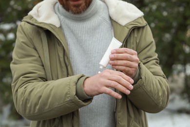 Photo of Man applying cream from tube onto hand outdoors, closeup. Winter care