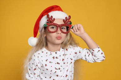 Photo of Girl wearing red decorative eyeglasses and Santa hat on orange background