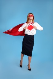 Photo of Confident businesswoman wearing superhero costume under suit on light blue background