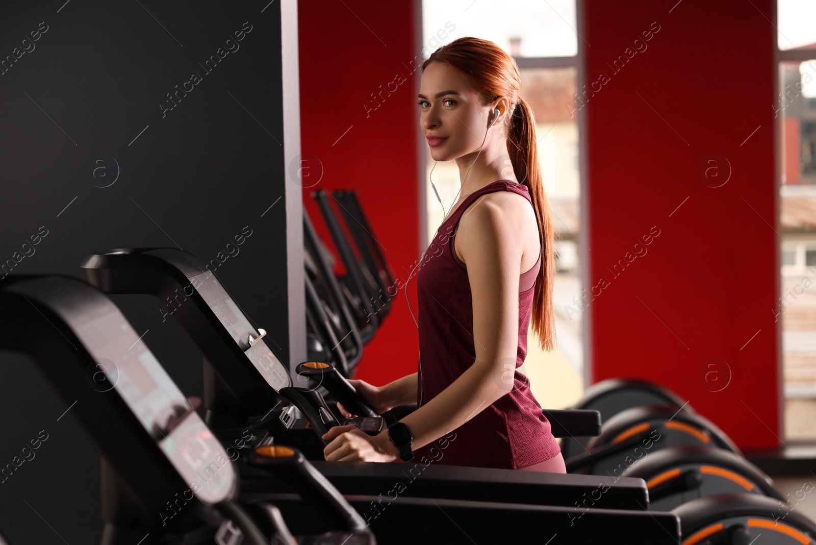 Photo of Athletic young woman with earphones training on treadmill in gym