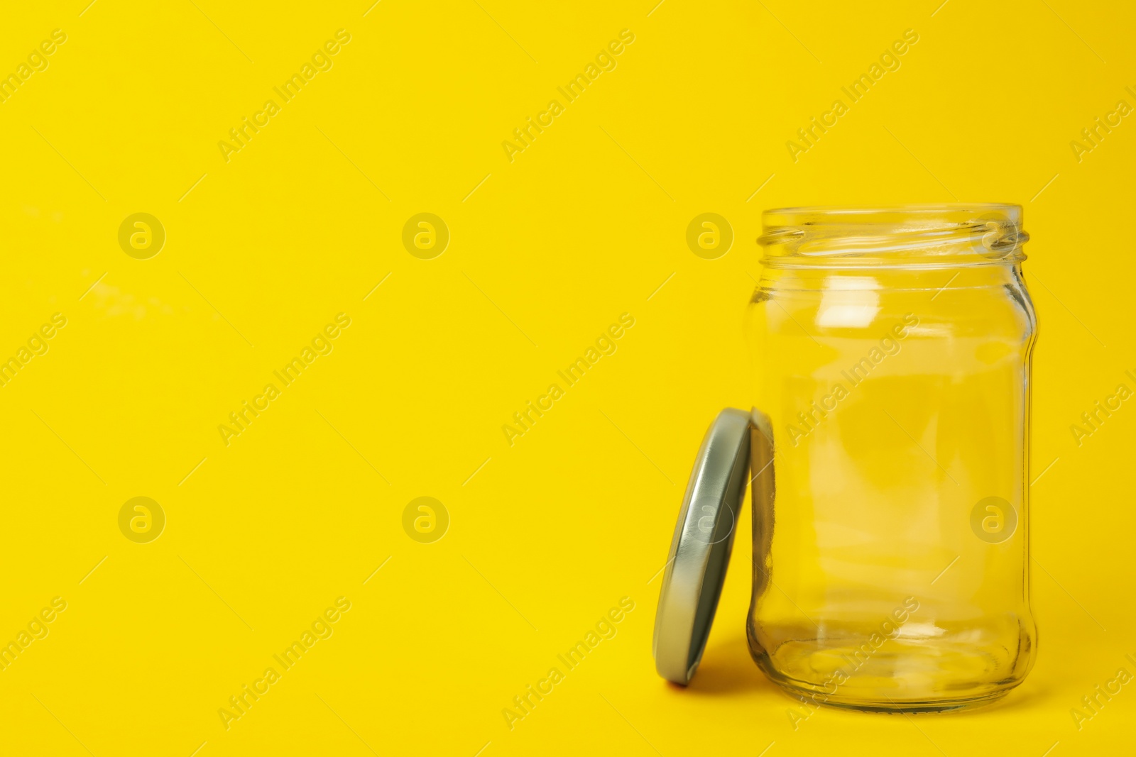 Photo of Open empty glass jar on yellow background, space for text