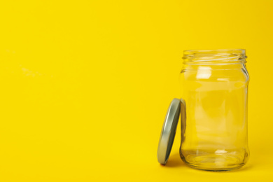 Photo of Open empty glass jar on yellow background, space for text