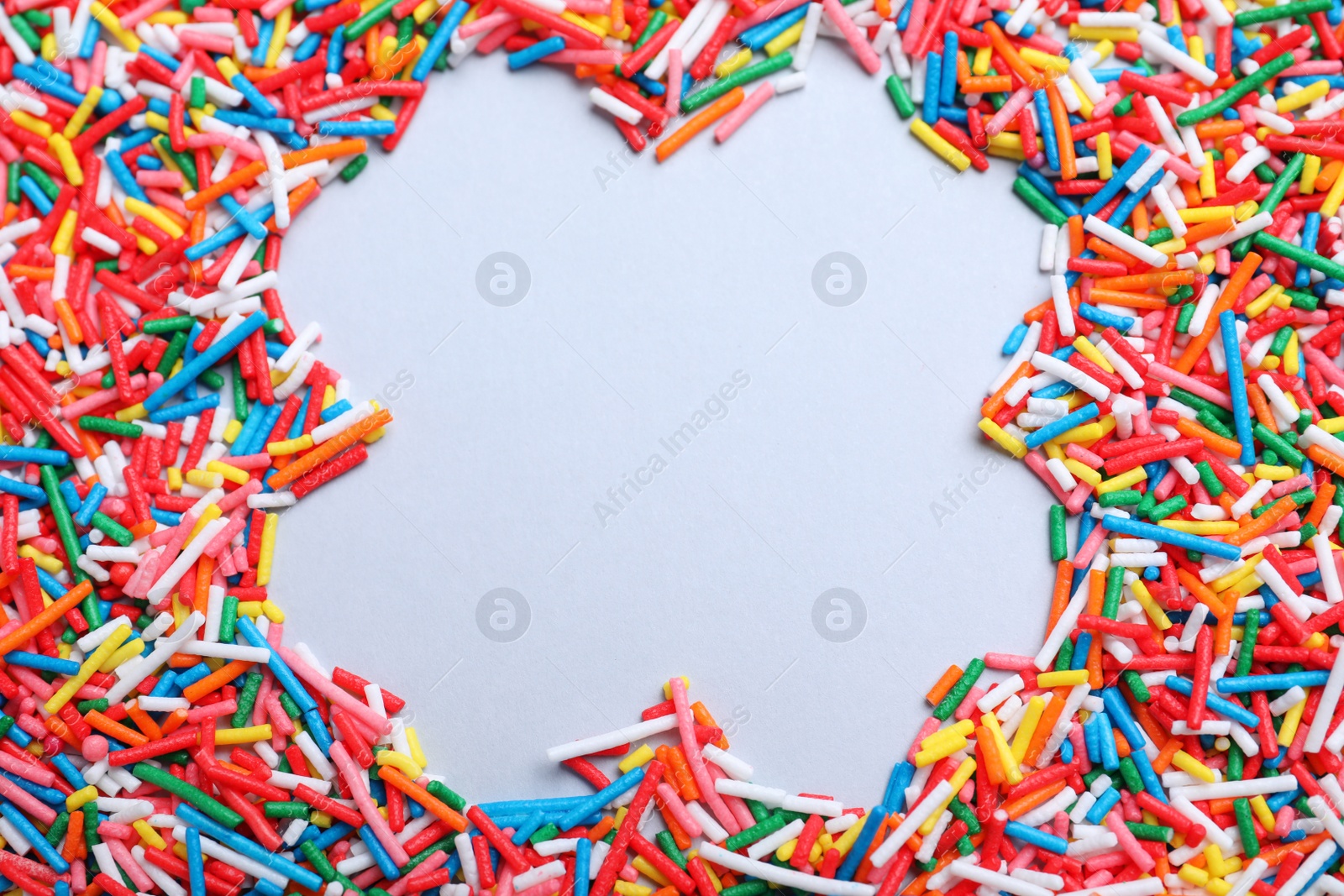 Photo of Frame of colorful sprinkles on light grey background, flat lay with space for text. Confectionery decor