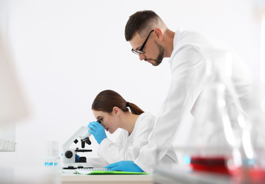 Photo of Scientist using microscope at table and colleague in laboratory. Medical research