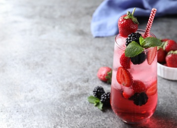 Photo of Delicious strawberry lemonade with soda water, mint and blackberries on grey table, space for text. Fresh summer cocktail