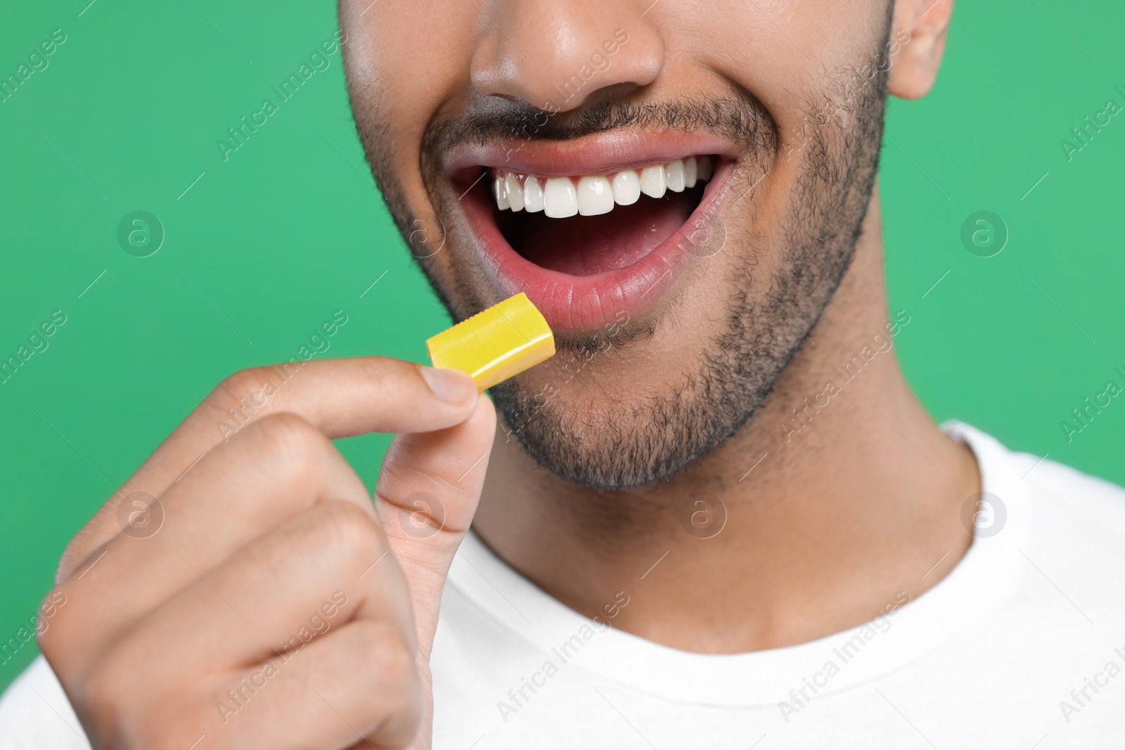 Photo of Happy man putting bubble gum into mouth on green background, closeup