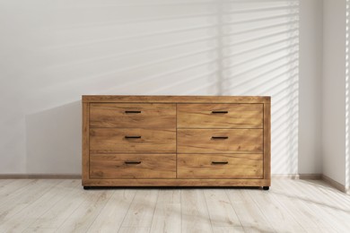 Photo of Wooden stylish chest of drawers near white wall indoors