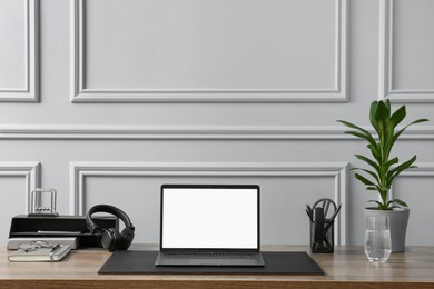 Photo of Stylish workplace with laptop, houseplant and stationery on wooden table near light grey wall