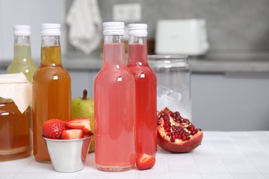 Photo of Tasty kombucha in glass bottles, jar and fresh fruits on white tiled table