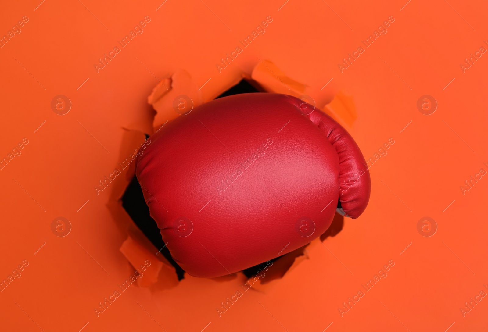 Photo of Man breaking through orange paper with boxing glove, closeup