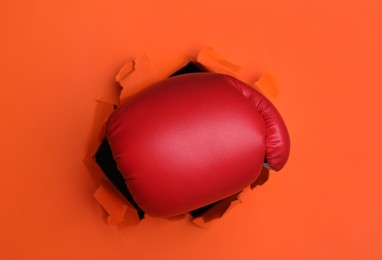 Photo of Man breaking through orange paper with boxing glove, closeup