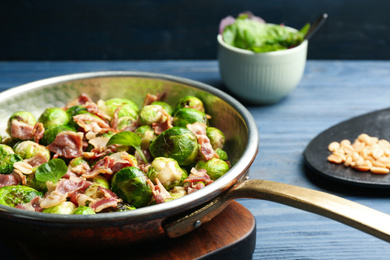 Photo of Delicious Brussels sprouts with bacon in frying pan on blue table, closeup